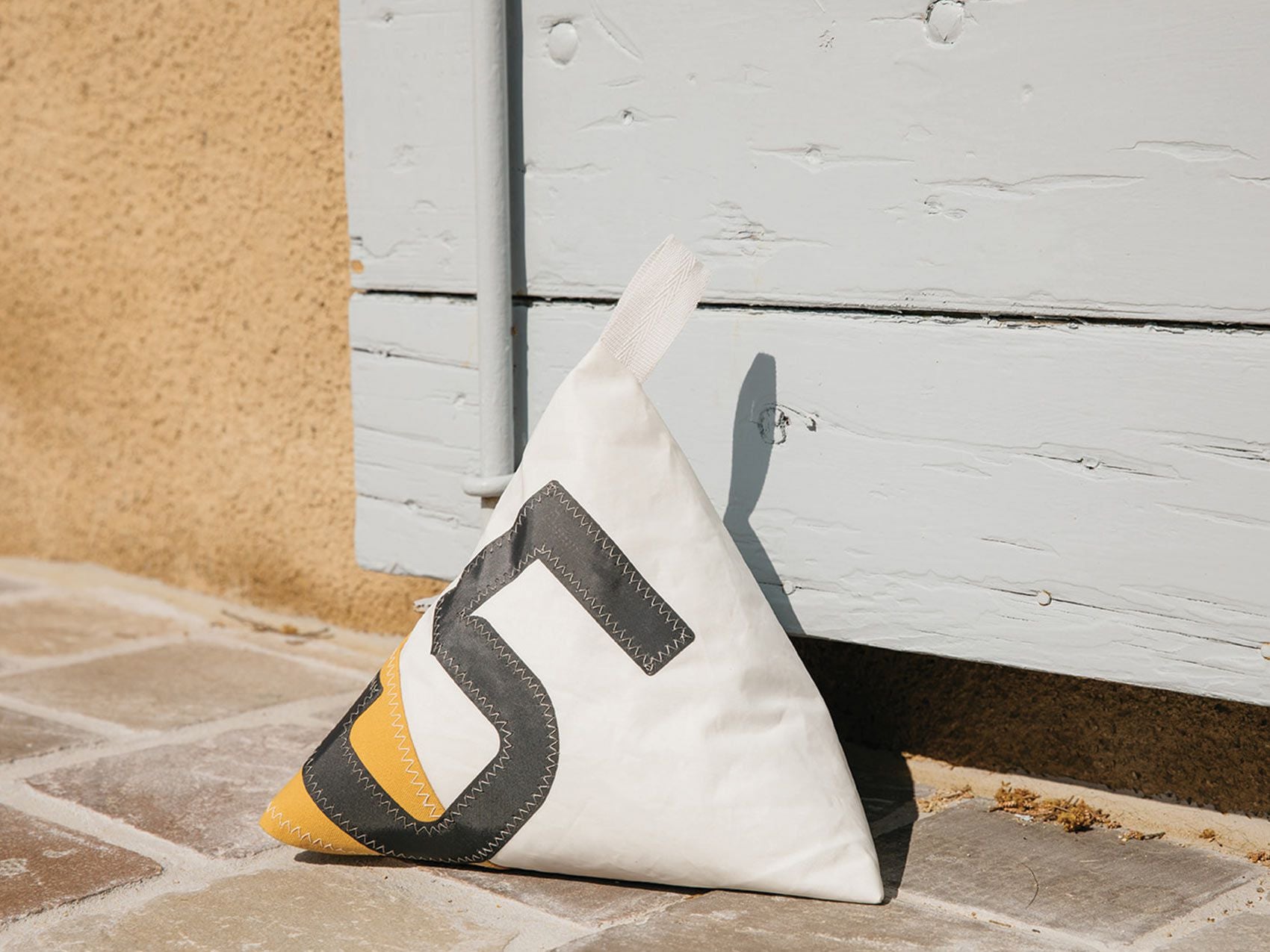 Made of white and grey Dacron sail, with yellow marine-grade canvas corner and adorned with an oversized grey number '5', this pyramid-shaped door stopper will add a splash of colour and nautical character to your interior!